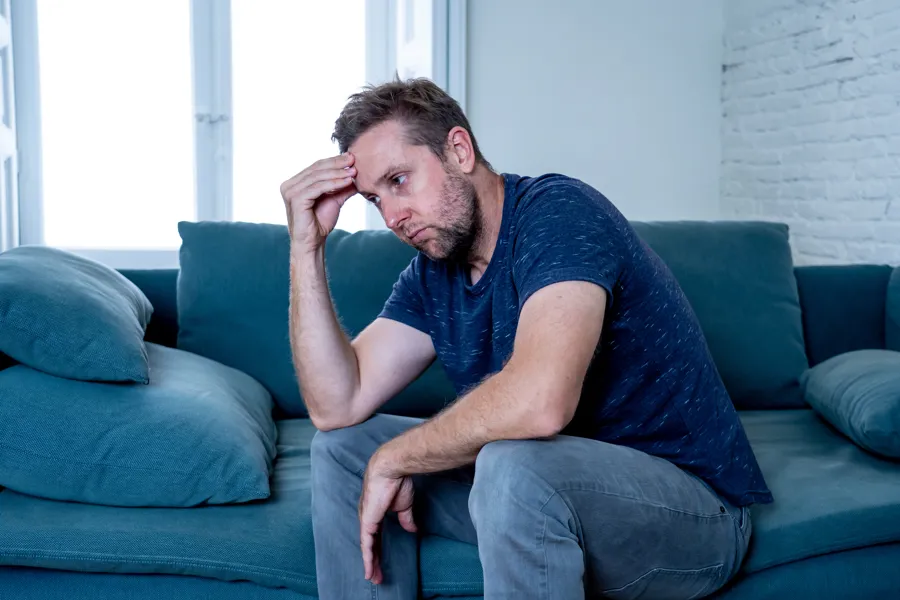 Bilde av en mann som sitter i en sofa, holder en hånd til pannen og ser deprimert ut