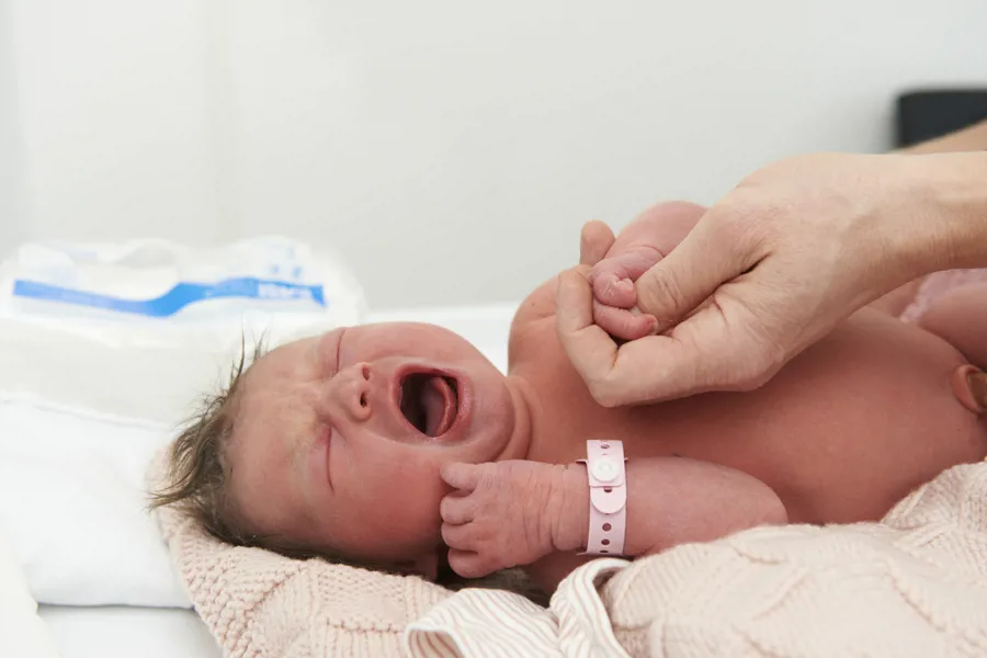 Bilde av nyfødt baby som gråter mens en voksen hånd holder babyen hånd
