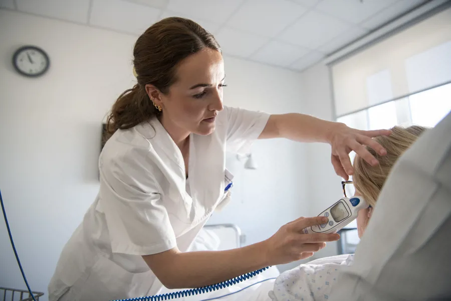 Bilde av en sykepleier som tar temperaturen på en pasient