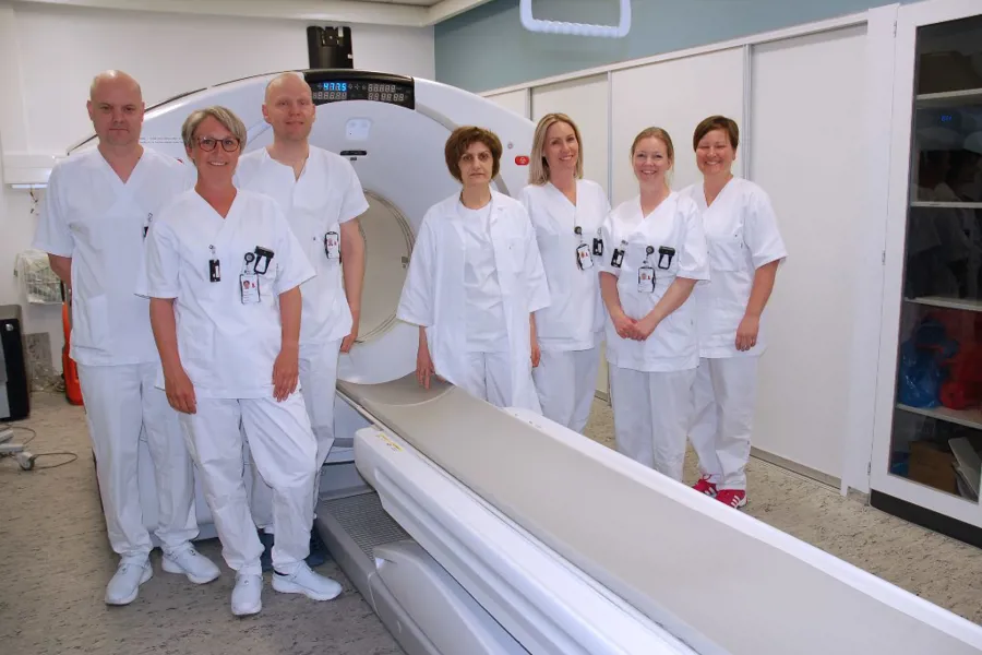 En gruppe mennesker i hvite labfrakker står foran en hvit maskin