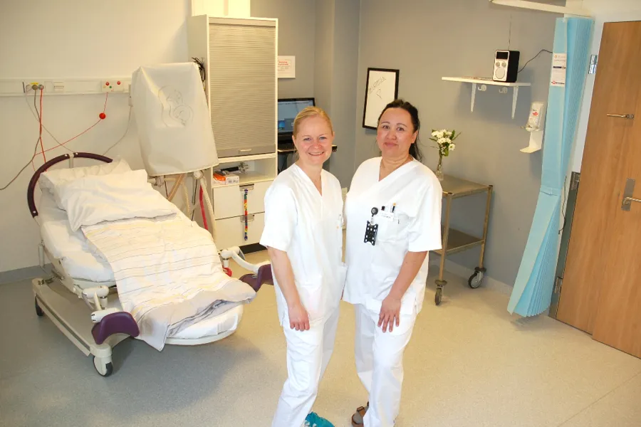 Et par kvinner i hvite labfrakker står ved siden av en pasient