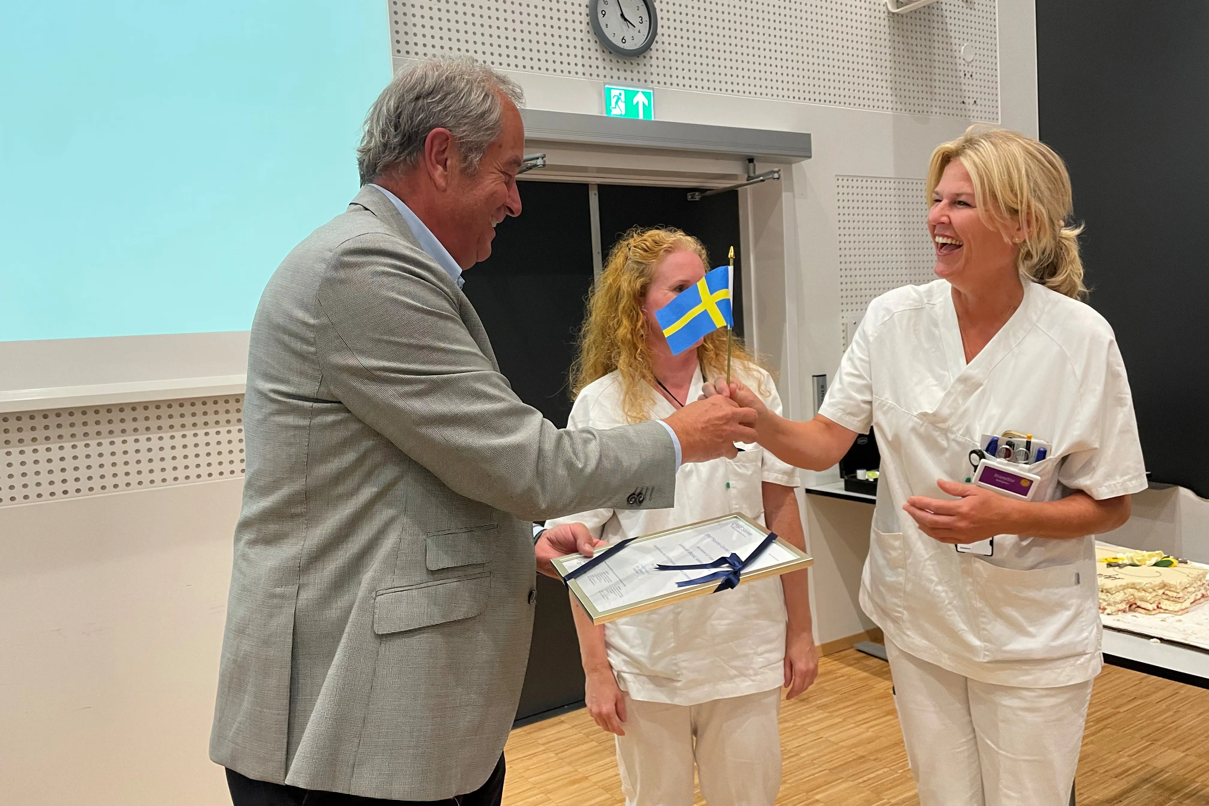 En sykepleier får et svensk flagg og et diplom av  professor Olle Ljungqvist