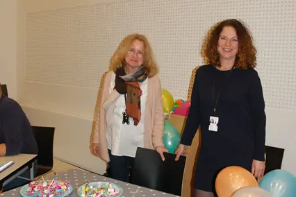 Et par kvinner som står ved siden av et bord med ballonger og et skilt