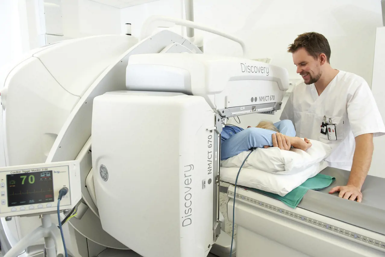 Pasient ligger i en CT-maskin og en radiolog passer på